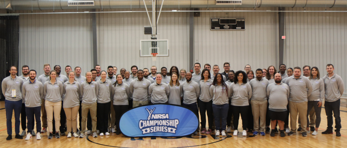 lineup of group of staff in front of banner on a basketball court