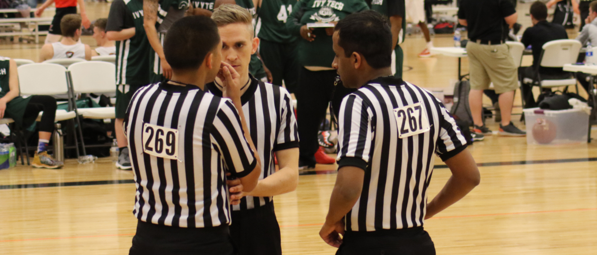 group of three basketball officials talking to to each other on a court