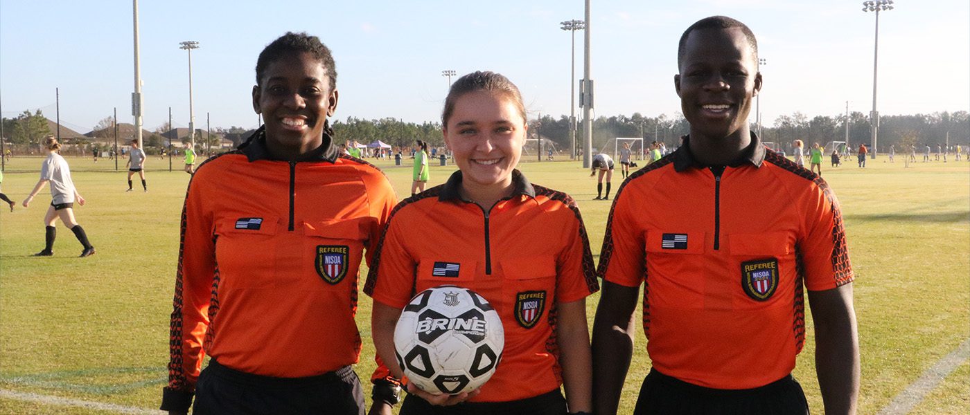 three soccer officials smiling with soccer ball in hands