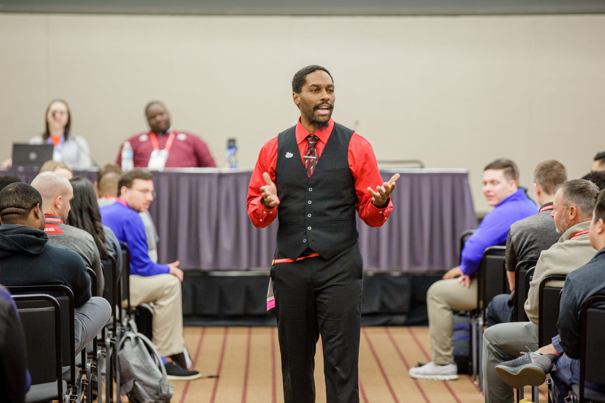 Kris Newsome speaking to a group of people while walking down the isle of a meeting room