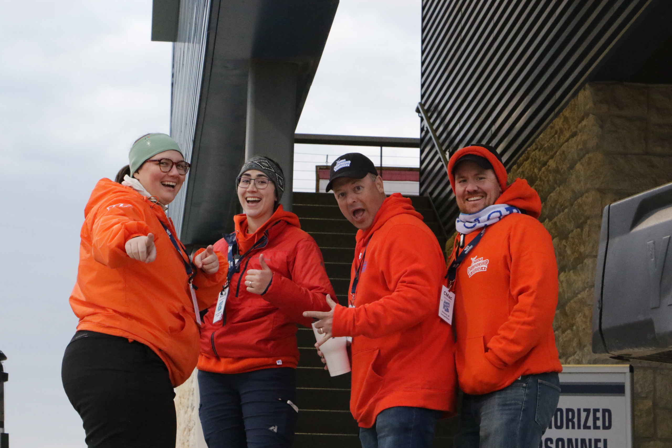 Four soccer staff in orange sweatshirts, smiling a camera